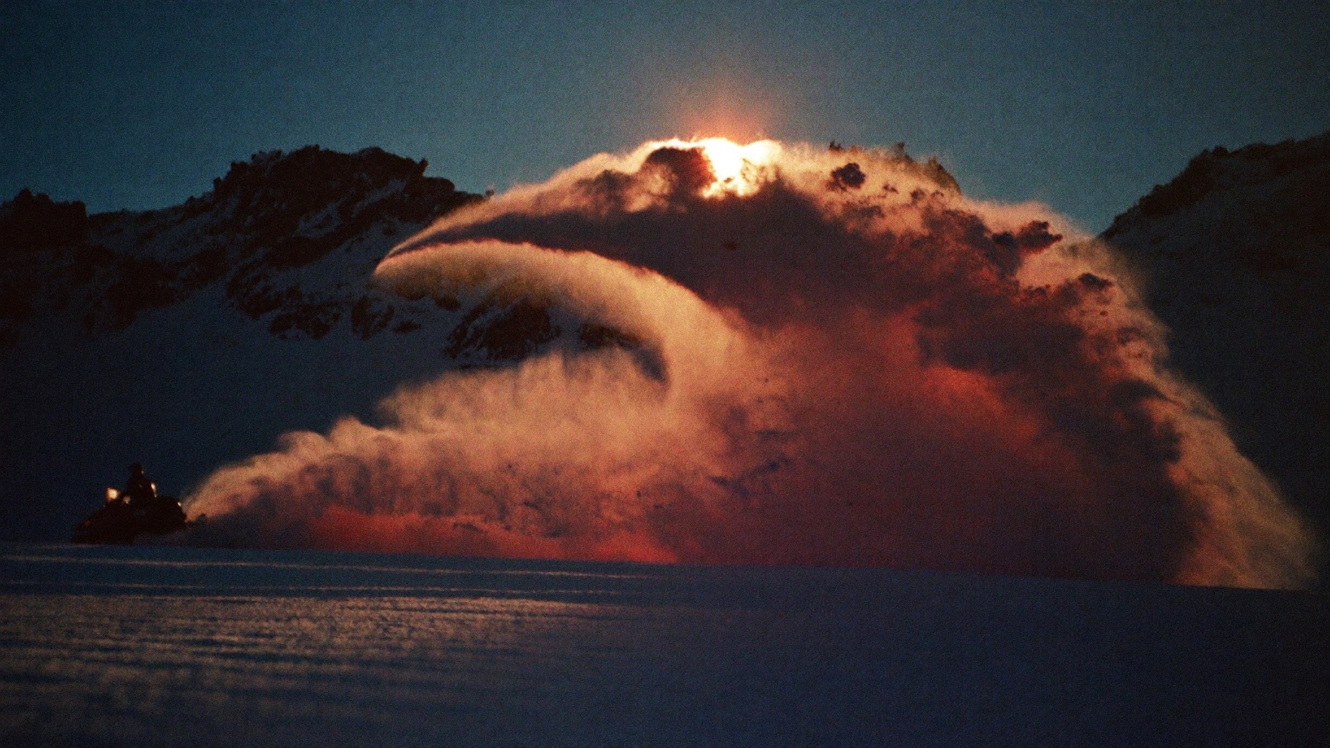 Snowmobile throwing a wave of powder lit by alpenglow