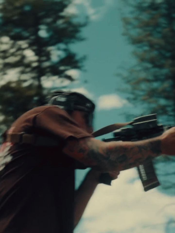 Crew member shouldering a rifle at the range, pines behind